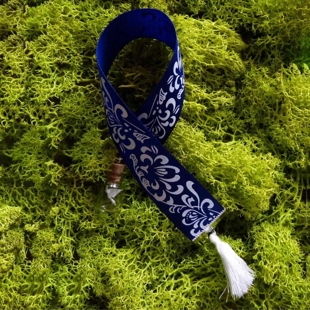 Blaues Band-Lesezeichen mit weißem floralen Muster, daran ein kleines Glasfläschchen mit gefaltetem Papier-Kranich.