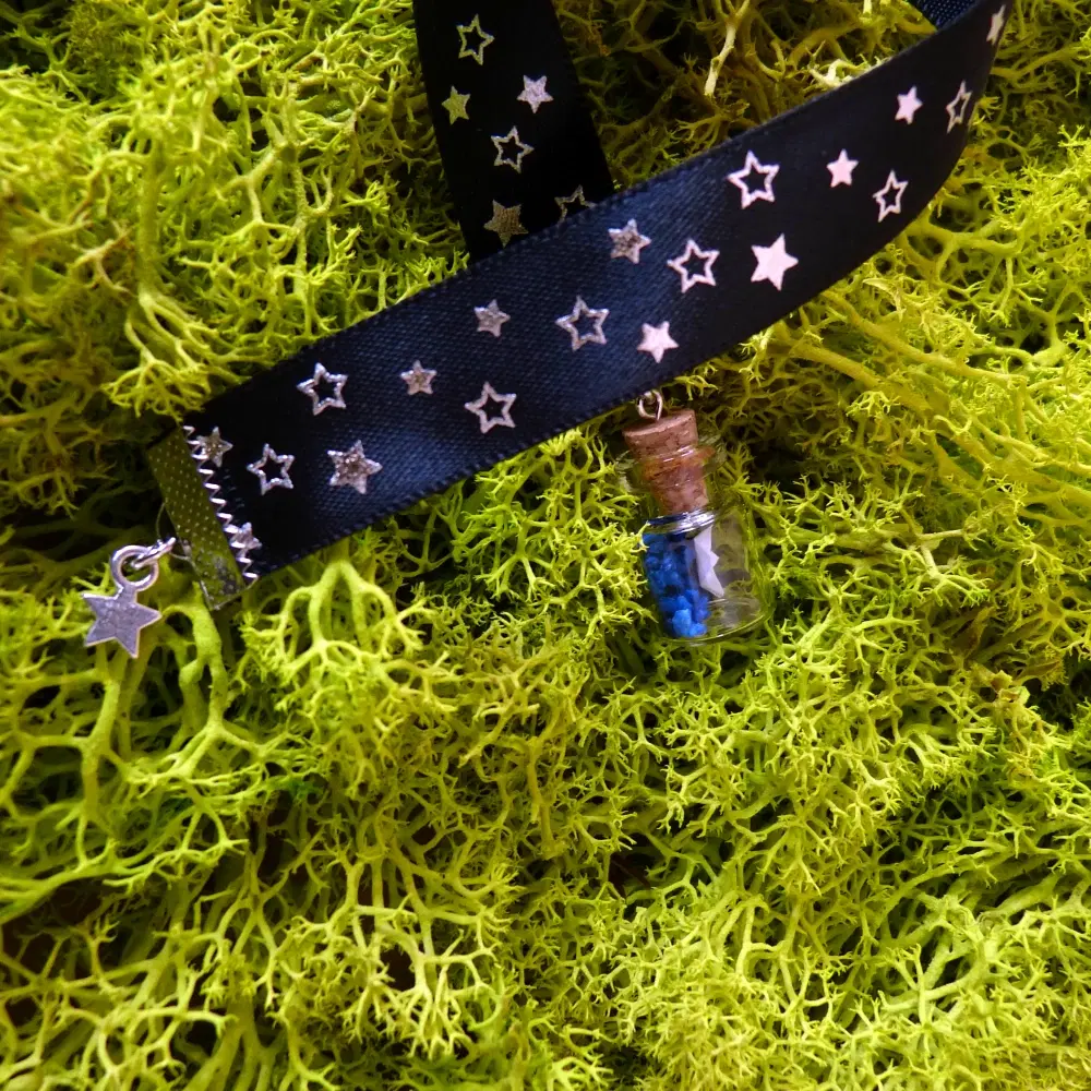 Blaues Band-Lesezeichen mit kleinen Sternen. Am Band hängen ein kleiner Sternanhänger sowie ein Glasfläschchen mit blauen Steinen und einem Papierschiff.