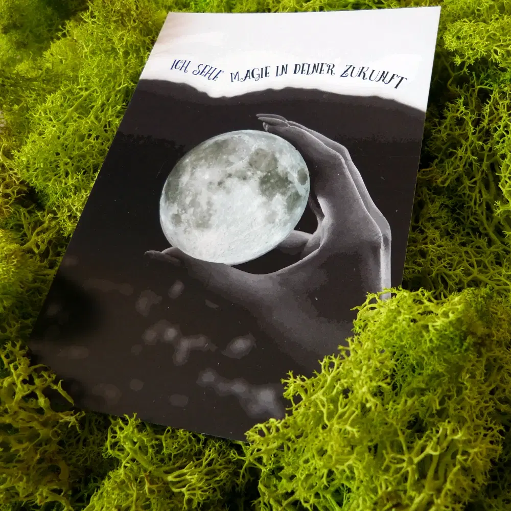 Postkarte mit einer Hand, die einen leuchtenden Vollmond hält. Über dem Motiv steht der Schriftzug "Ich sehe Magie in deiner Zukunft".