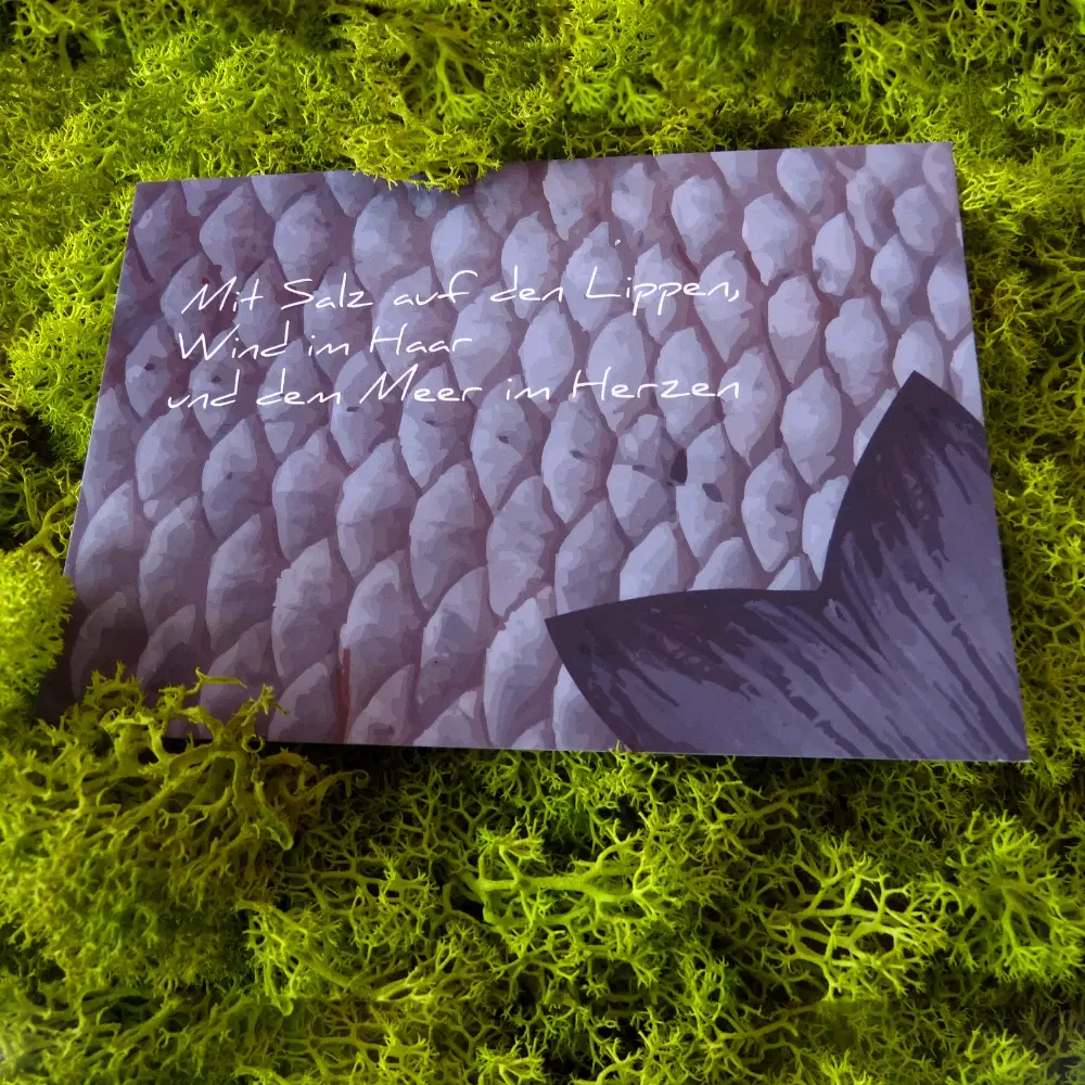 Postkarte mit stilisiertem Fischschuppenmuster und dunkler Flosse auf der rechten Seite. Darauf steht der Spruch "Mit Salz auf den Lippen, Wind im Haar und dem Meer im Herzen".